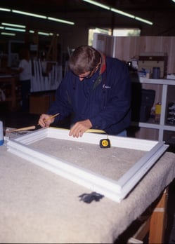 man measuring window frame in manufacturing factory