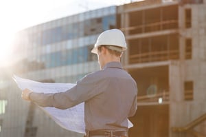 professional looking at blueprint in front of a building under construction