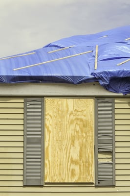 House repairs after tornado Boarded window beneath roof with protective sheets of blue plastic