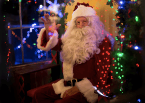 Santa waving in front of window and Christmas tree
