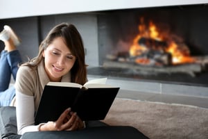 Portrait of beautiful woman reading energy efficiency book by fireplace
