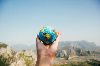 person holding a tiny globe over landscape view